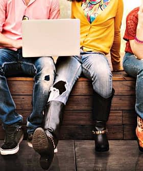 A group of young individuals sitting side by side, engaged with various devices and wearing casual clothing. - Olive Oil Times
